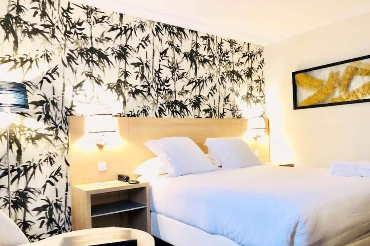 Ein Hotelzimmer mit Bett, Nachttischen, einem Sessel und einer Wand mit Bambusmuster.