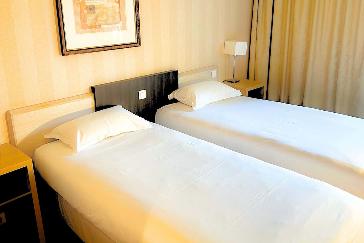 Ein Hotelzimmer mit zwei Einzelbetten, einem Nachttisch mit Lampe und einem gerahmten Bild an der Wand.