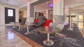 A modern lobby with seating areas, a digital display, and a carpet with motivational text. - Hôtel Inn Paris CDG Airport (Roissy-en-France)