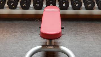 A gym with a bench, dumbbells, and a clock on the wall.