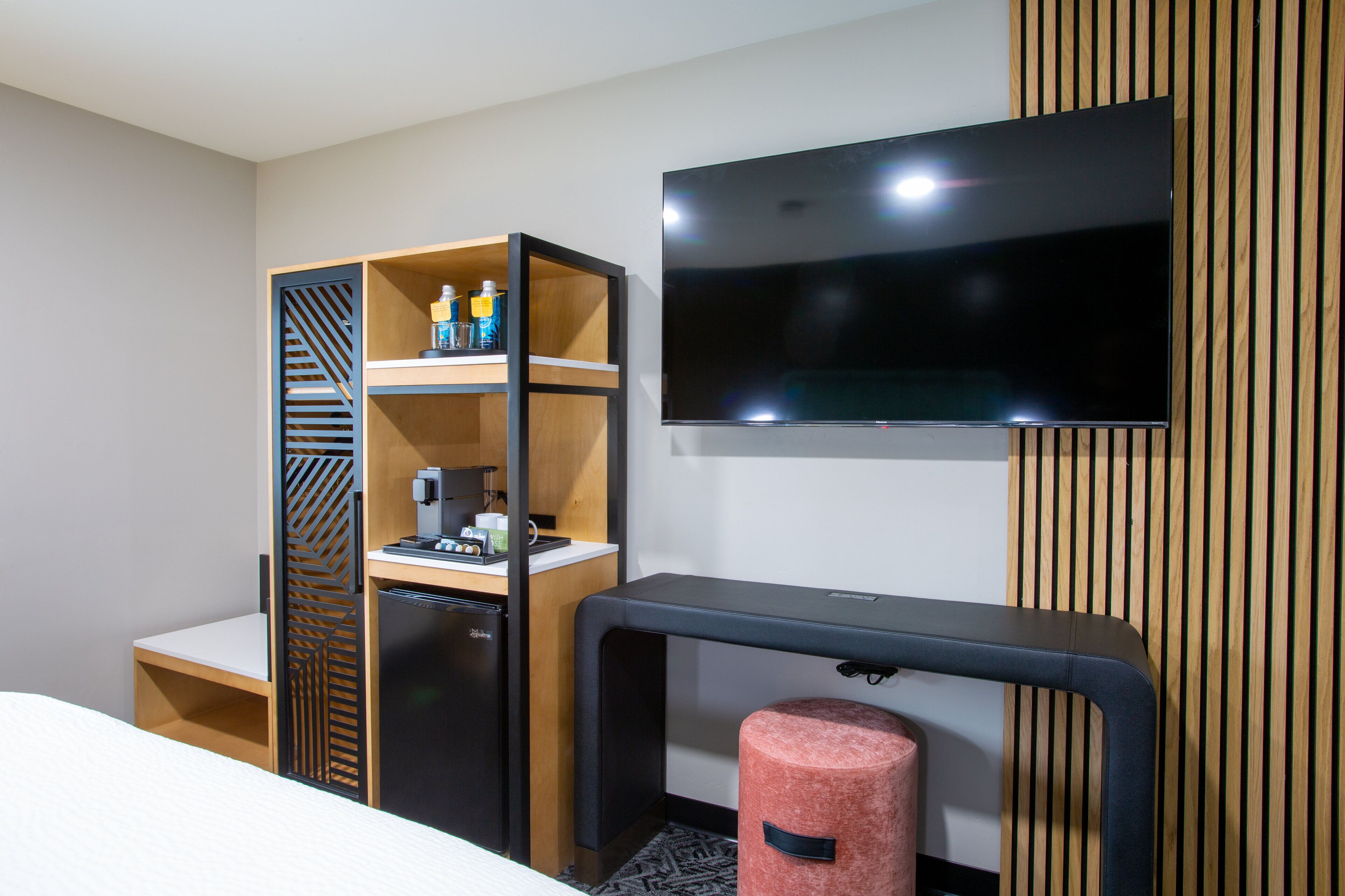 Ein Hotelzimmer mit einem Bett, einem Schreibtisch mit Computer, einem Fernseher, einer Minibar und einem kleinen Kühlschrank.