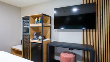Ein Hotelzimmer mit einem Bett, einem Schreibtisch mit Computer, einem Fernseher, einer Minibar und einem kleinen Kühlschrank.
