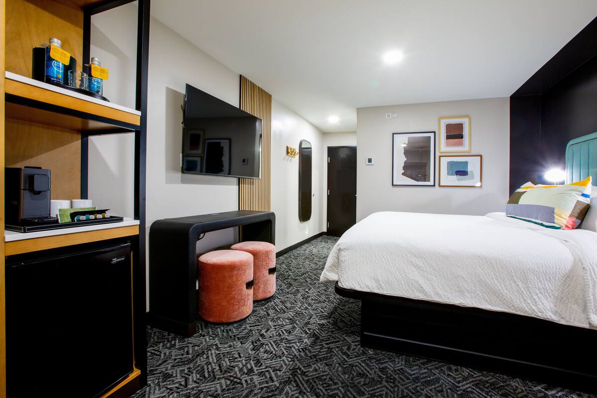 Habitación de hotel con cama, escritorio con computadora, refrigerador pequeño y televisor en la pared.