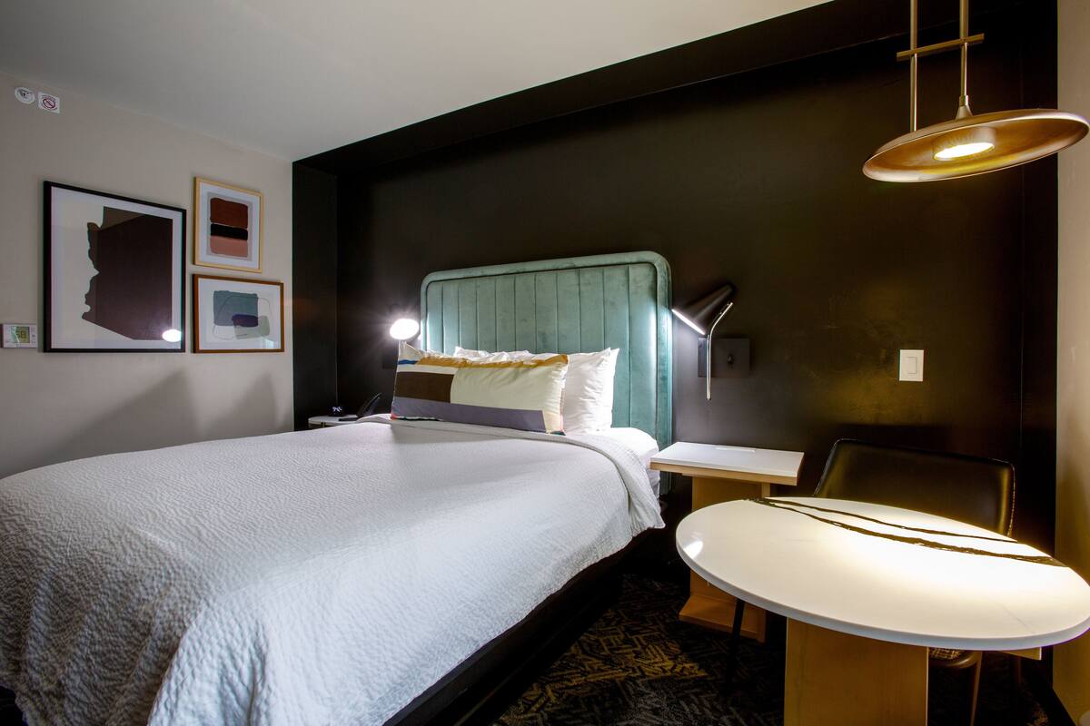 Una habitación de hotel con una cama grande, un escritorio con lámpara y una silla.