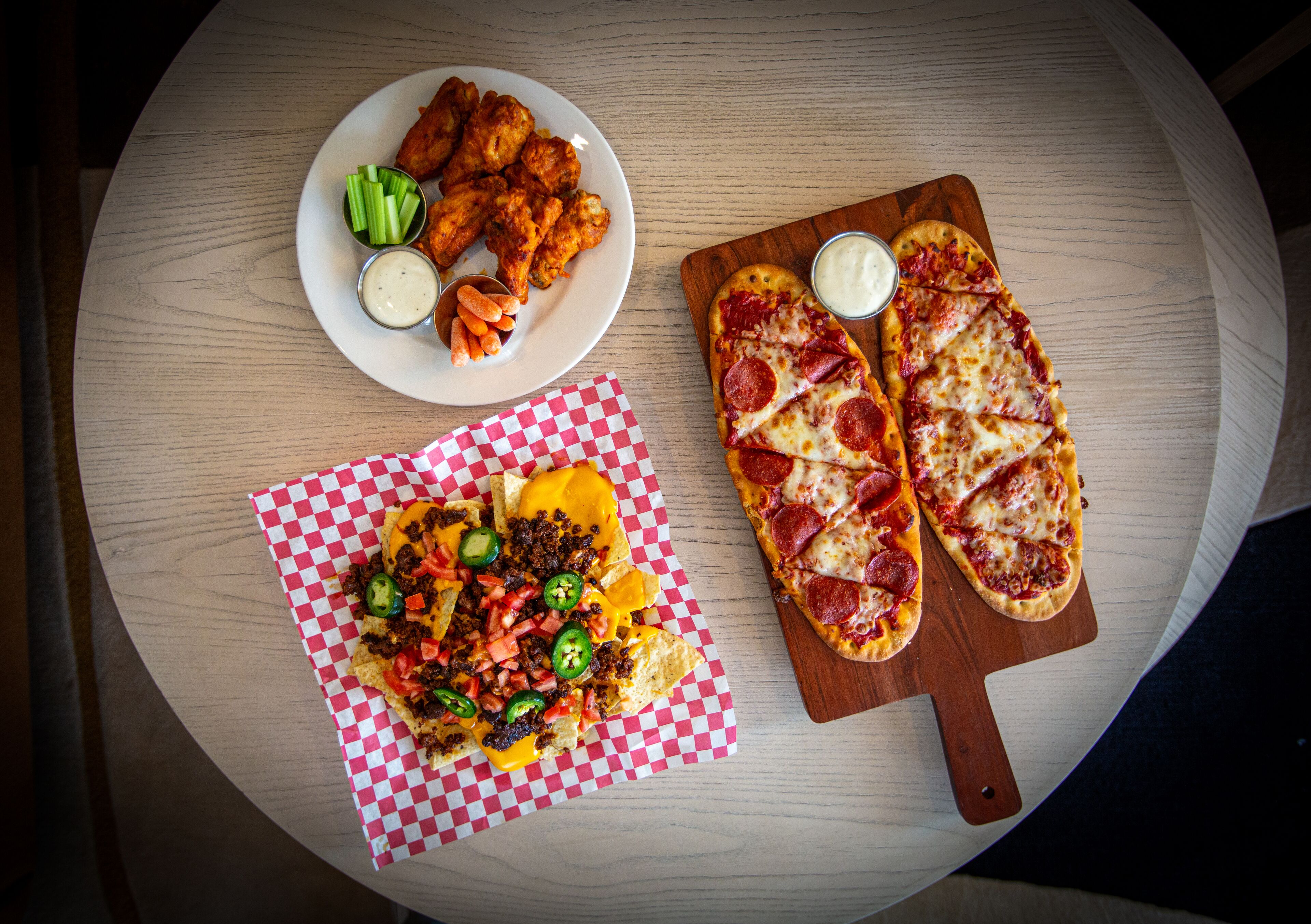 A table with a pizza, nachos, and chicken wings.
