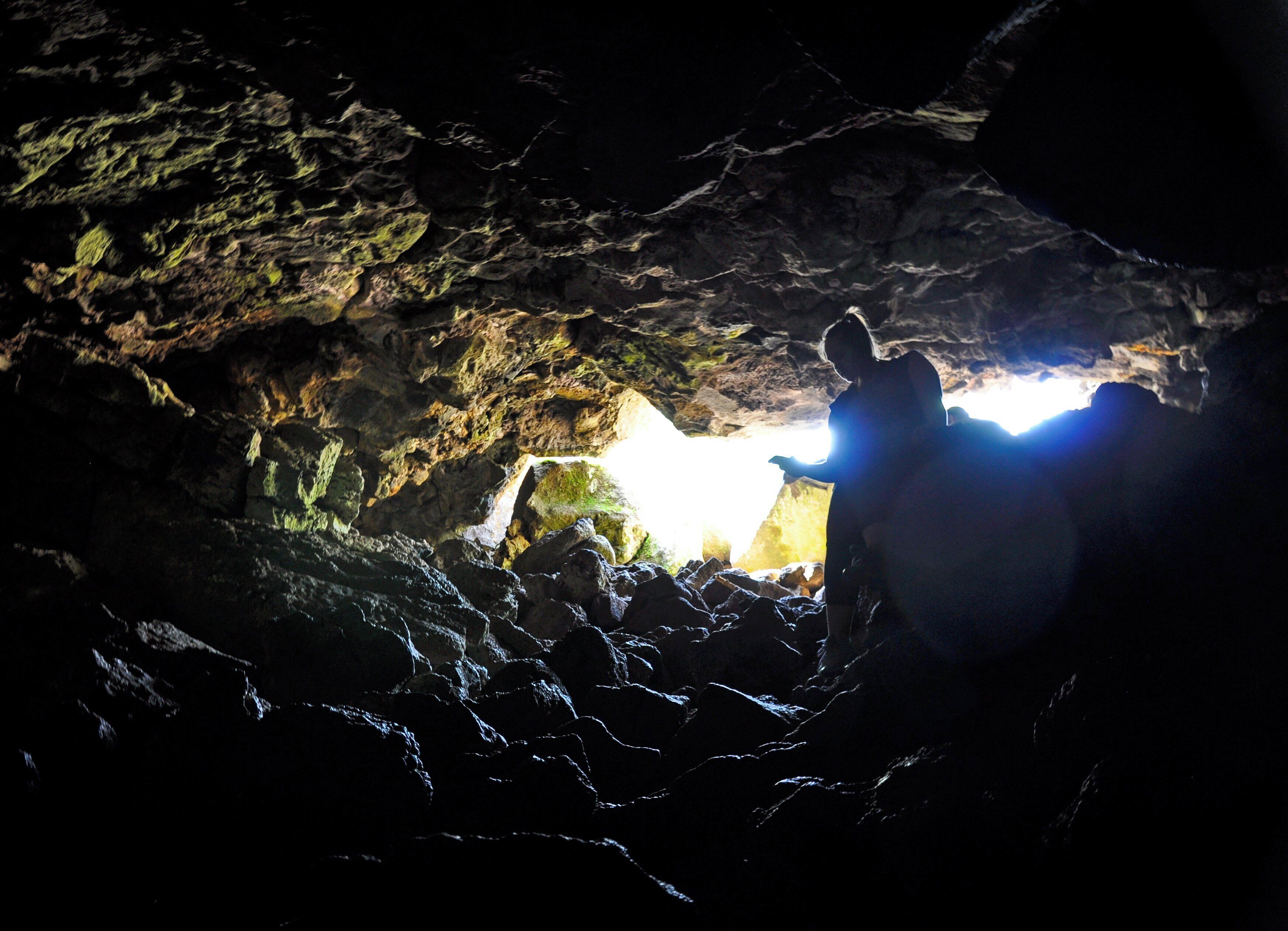 A cave interior with rough rock formations and a person standing near a light source.