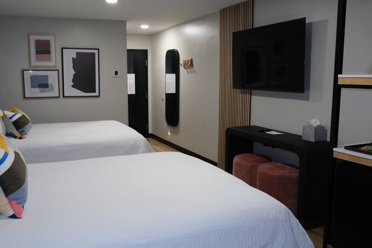 Habitación de hotel con dos camas, un escritorio, un televisor y obras de arte en las paredes.