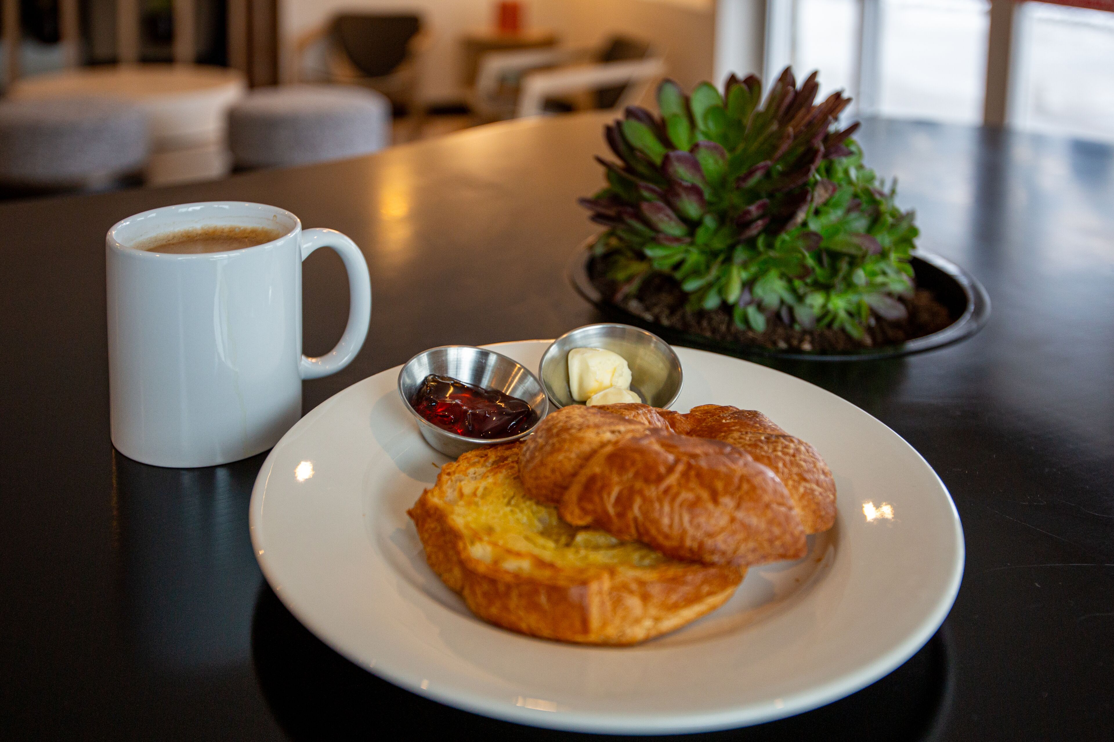 Un plato con un croissant y una taza de café sobre una mesa.