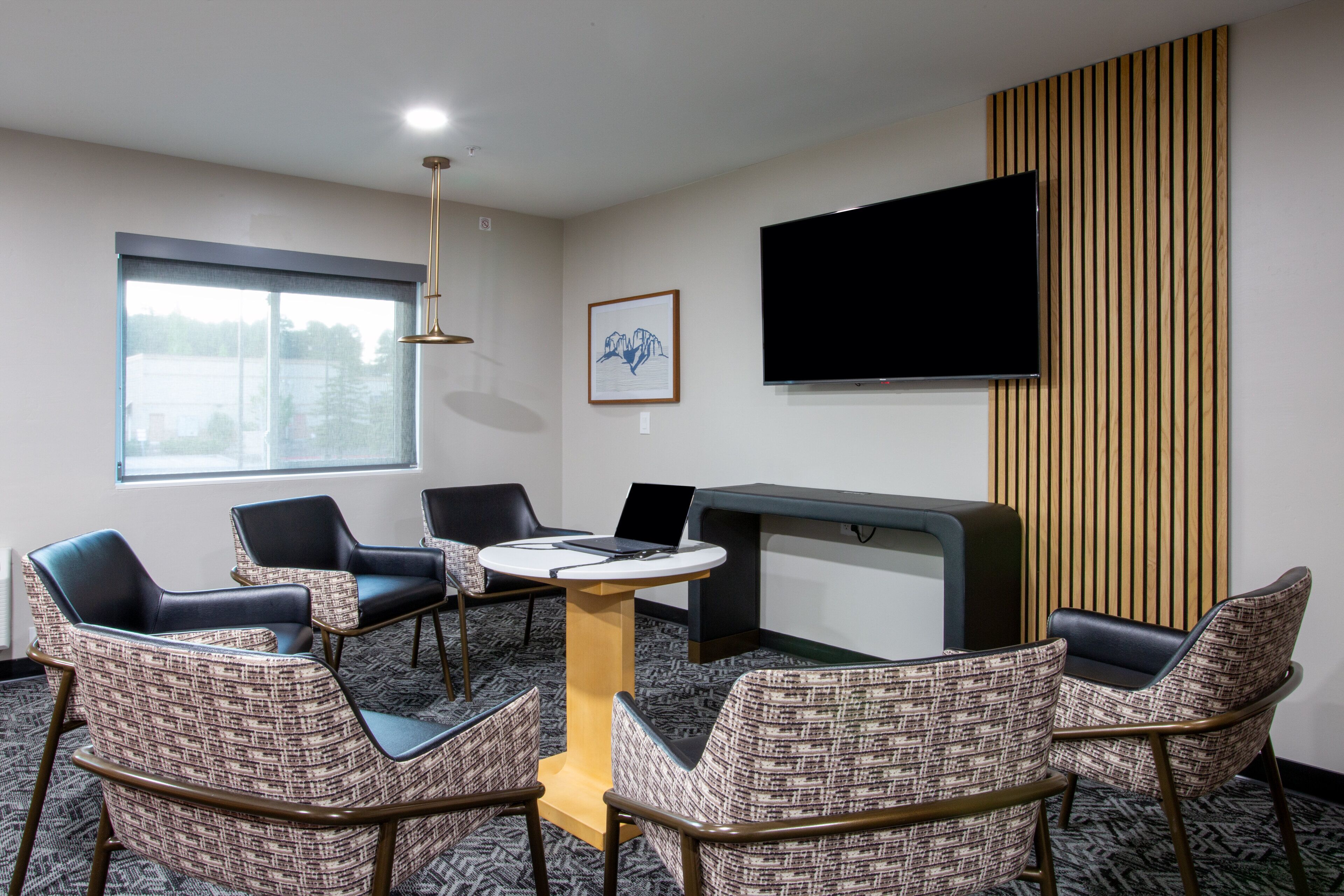 A conference room with a round table, four chairs, a flat-screen TV, and a window with blinds.