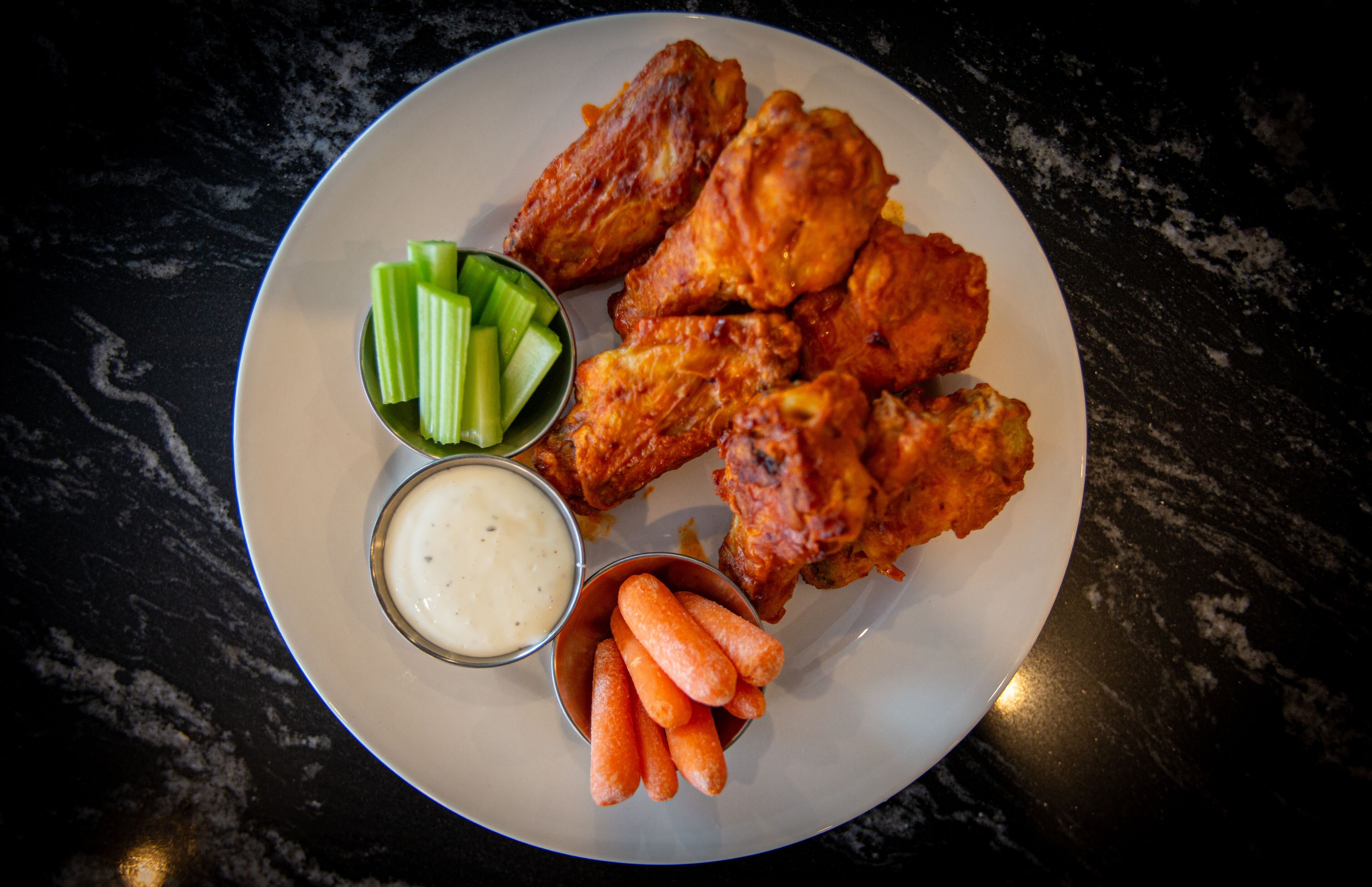 Une assiette d’ailes de poulet accompagnées de bâtonnets de céleri et de carottes, et deux sauces pour tremper.
