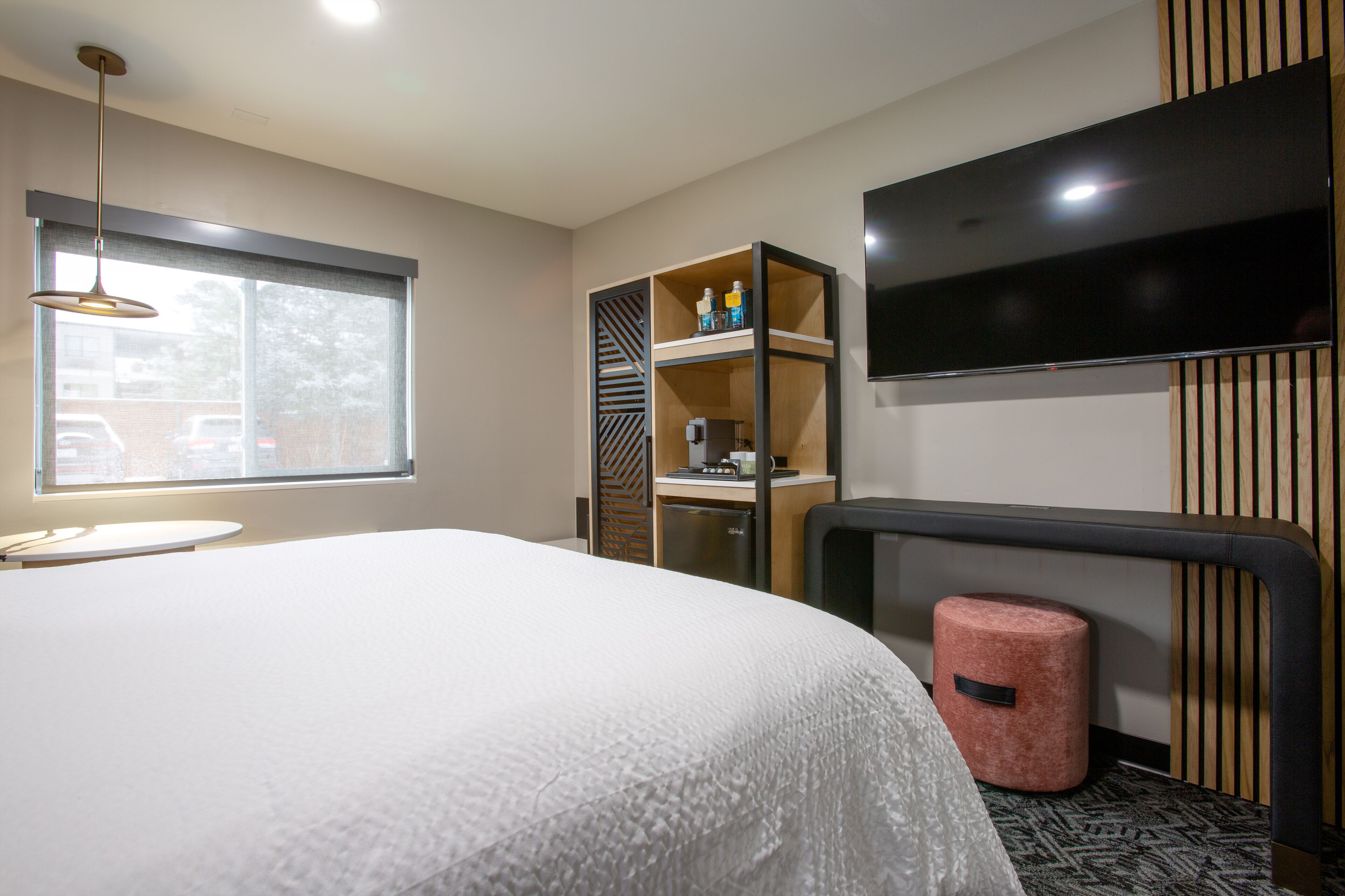 Habitación de hotel con cama, televisión montada en la pared, escritorio con silla y ventana con vistas al exterior.