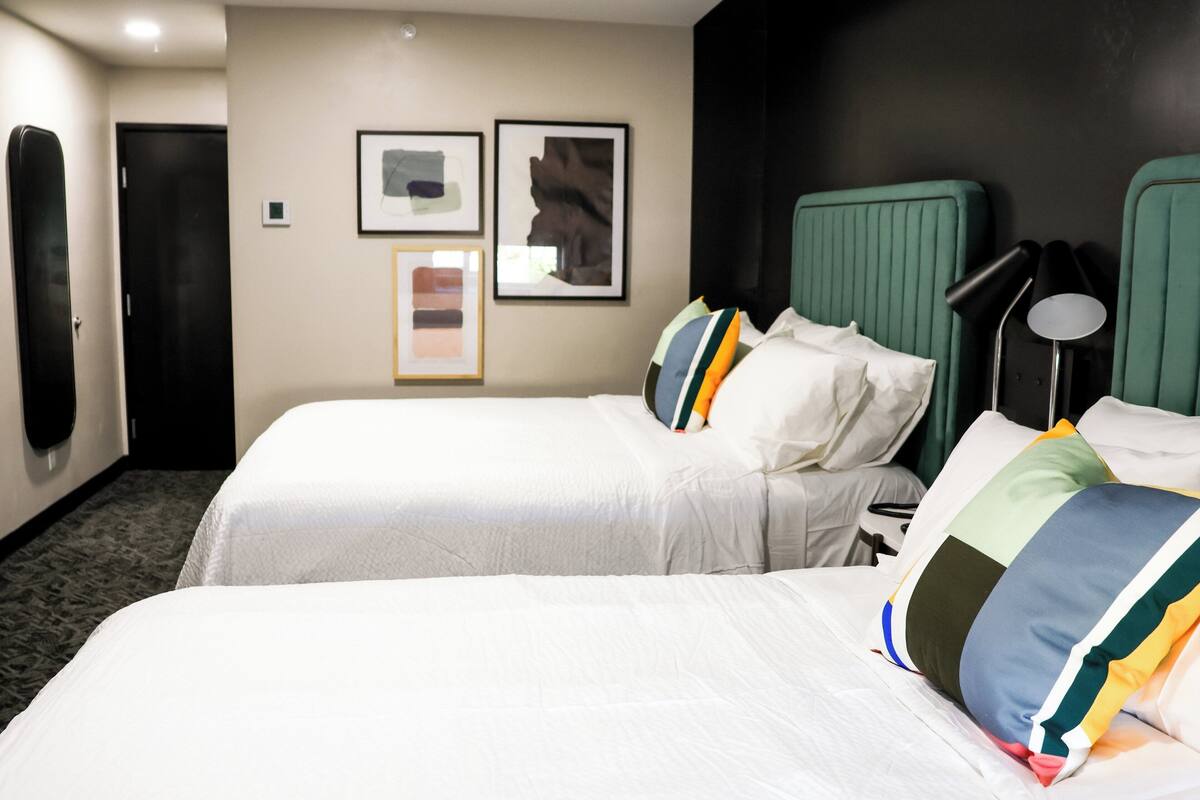 Habitación de hotel con dos camas, una puerta y cuadros en la pared.