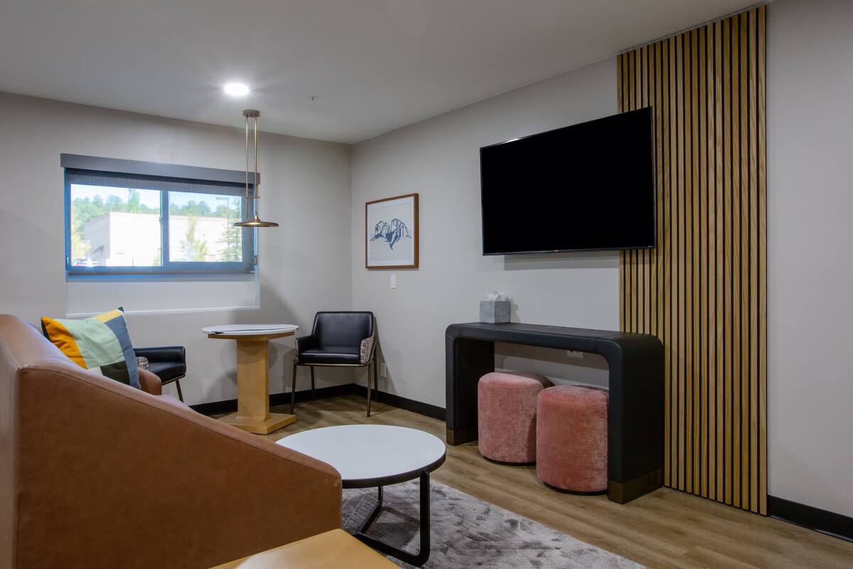 Una sala de estar moderna con un sofá, una mesa redonda, una silla, una mesita, otomanas, un televisor y una ventana con vistas.