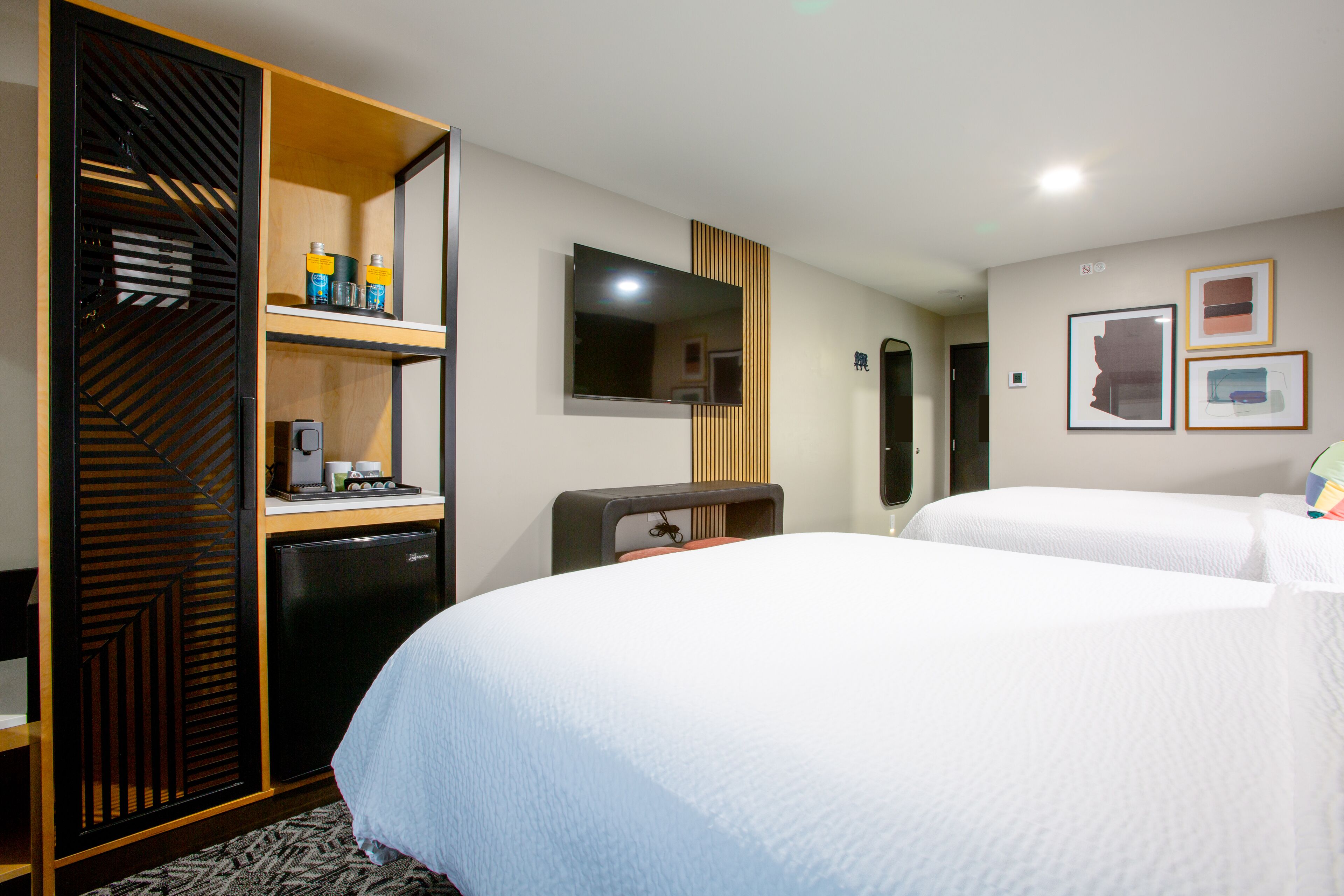 A hotel room with two beds, a desk with a computer, a minibar, and a TV.