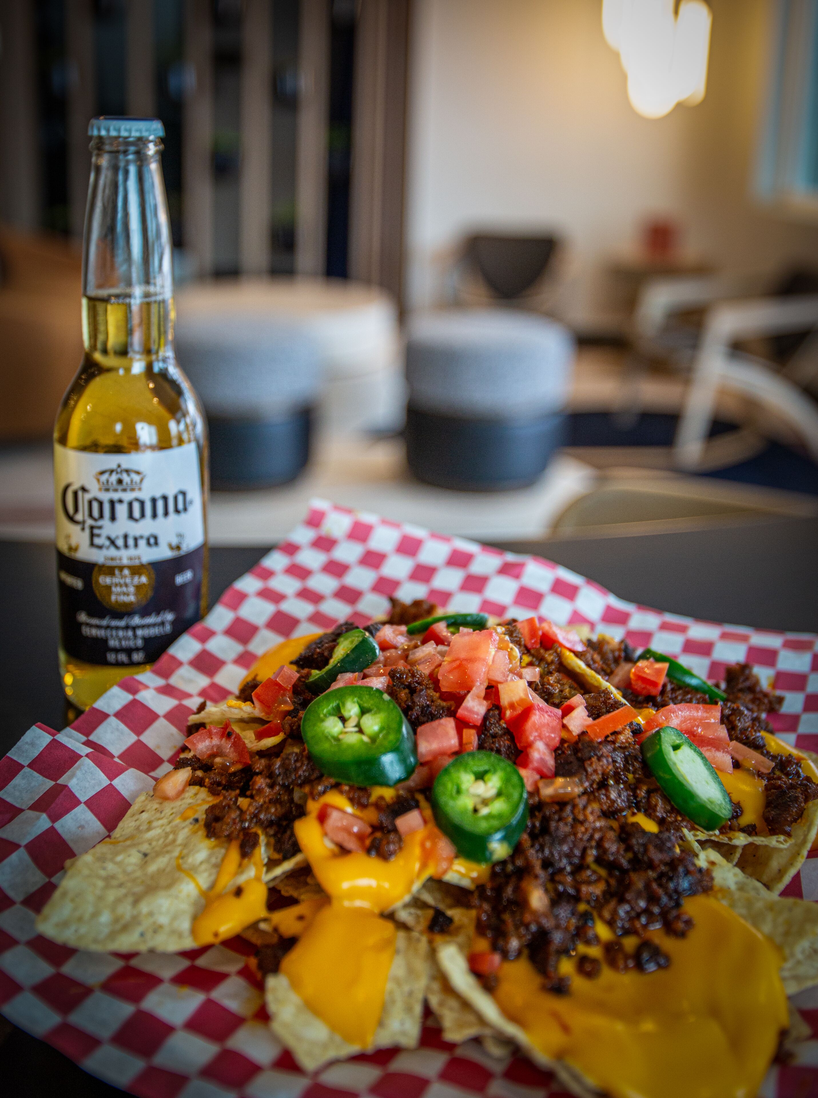 Nachos with toppings and a bottle of Corona Extra beer on a table.