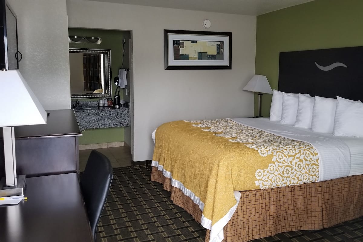 A hotel room with a bed, bedside tables, a desk, and a bathroom visible through an open door.