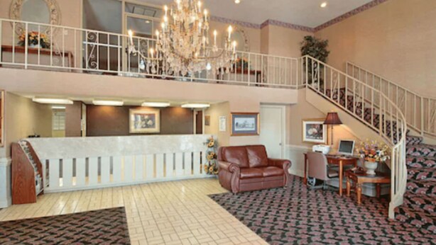 A spacious lobby with a chandelier, a staircase, a reception desk, and a leather sofa. - Days Inn by Wyndham West Memphis (West Memphis)