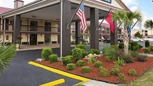 A Days Inn with a covered entrance, American flags, and landscaped garden area. - Days Inn by Wyndham West Memphis (West Memphis)