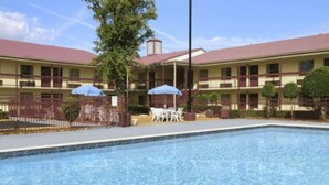 A hotel with a swimming pool, outdoor seating, and a two-story building with a red roof. - Days Inn by Wyndham West Memphis (West Memphis)