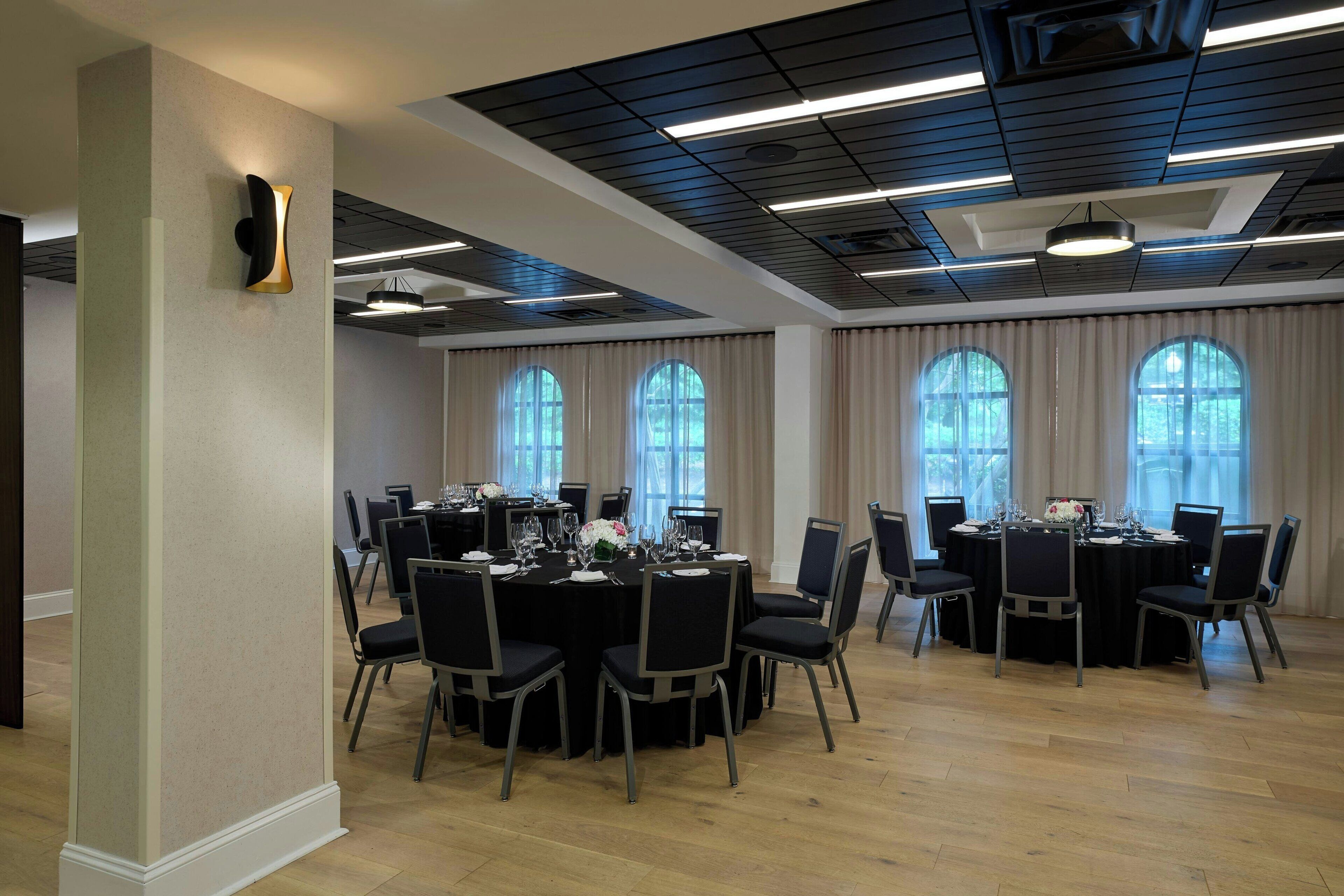 A conference room with round tables, black chairs, and large windows with curtains.