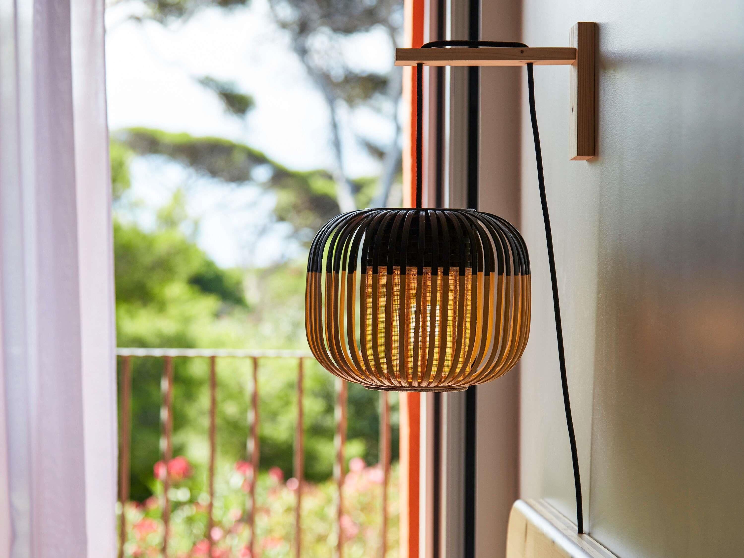 A pendant light with a black and gold design, hanging from a wooden bracket on a white wall.