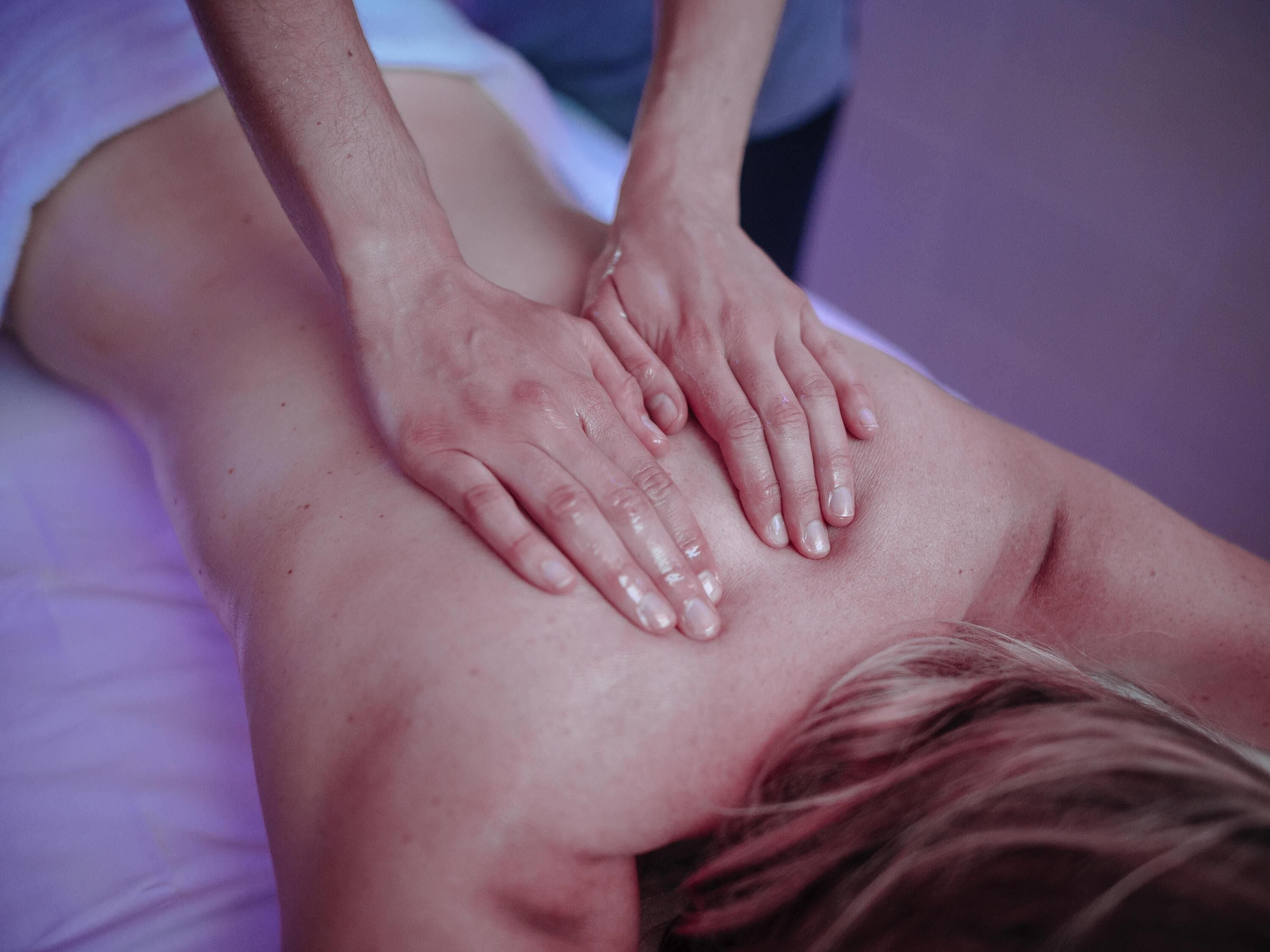 A massage therapy session with a focus on hands applying pressure to a client's back.