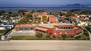 Un quartier résidentiel en bord de mer, caractérisé par un imposant bâtiment rouge, une plage avec des transats et une vue sur l’océan et les montagnes lointaines.
