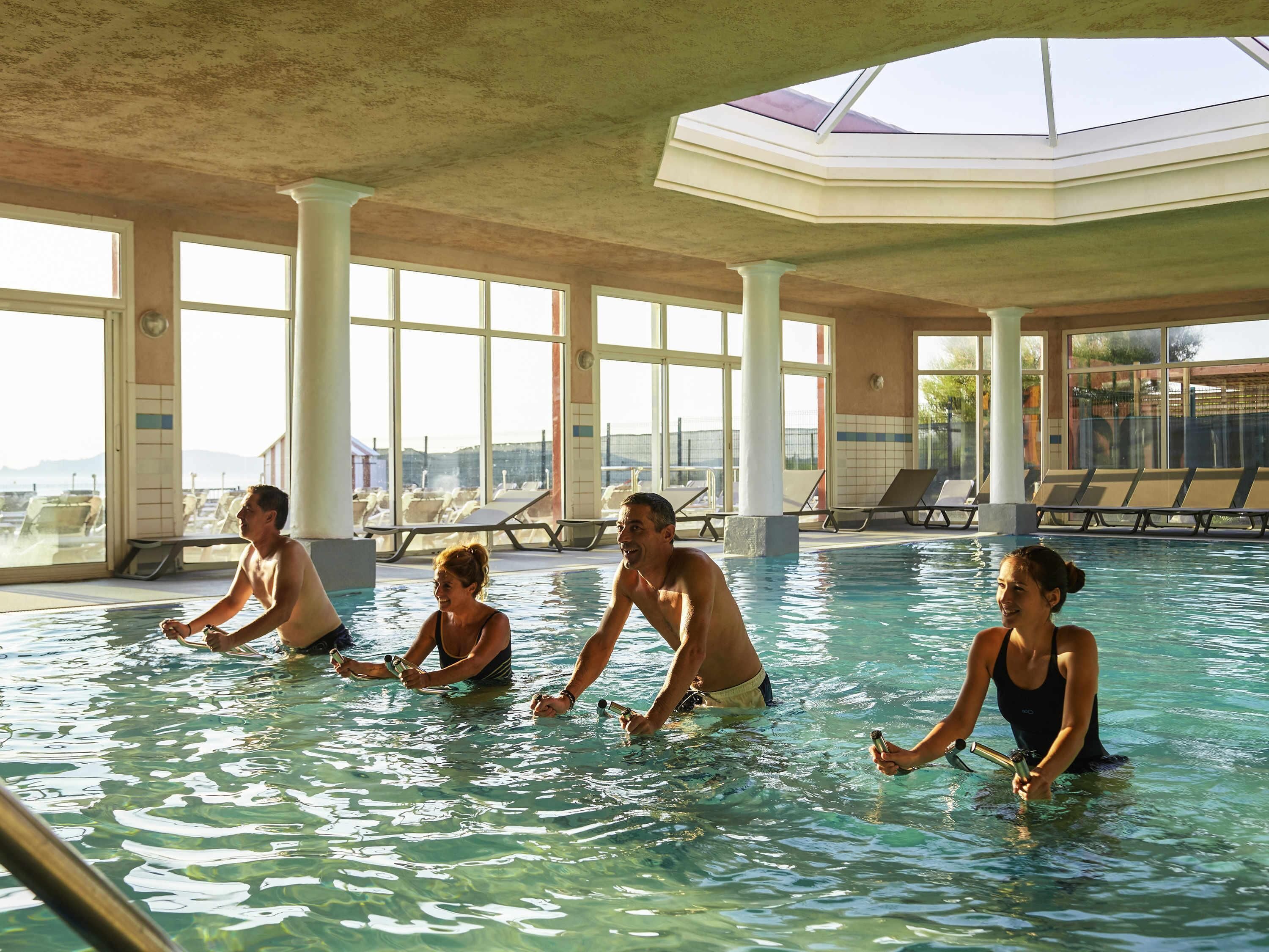 Una piscina interior con agua cristalina, ventanas amplias y sillones de descanso.