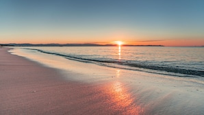 Une plage au coucher du soleil, avec des vagues calmes et un ciel dégagé.