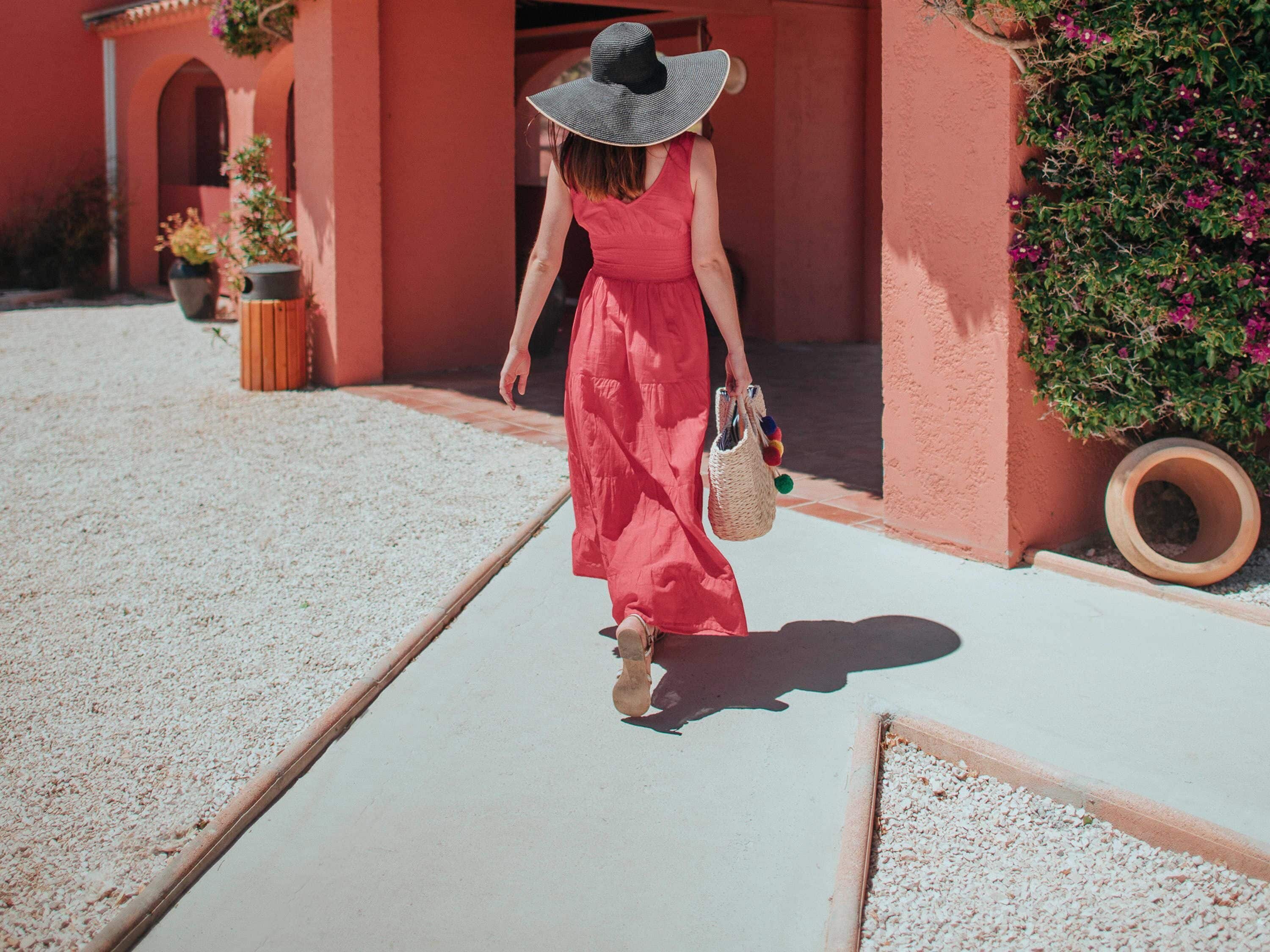 Una mujer con un vestido rojo y un sombrero de ala ancha camina por un sendero.