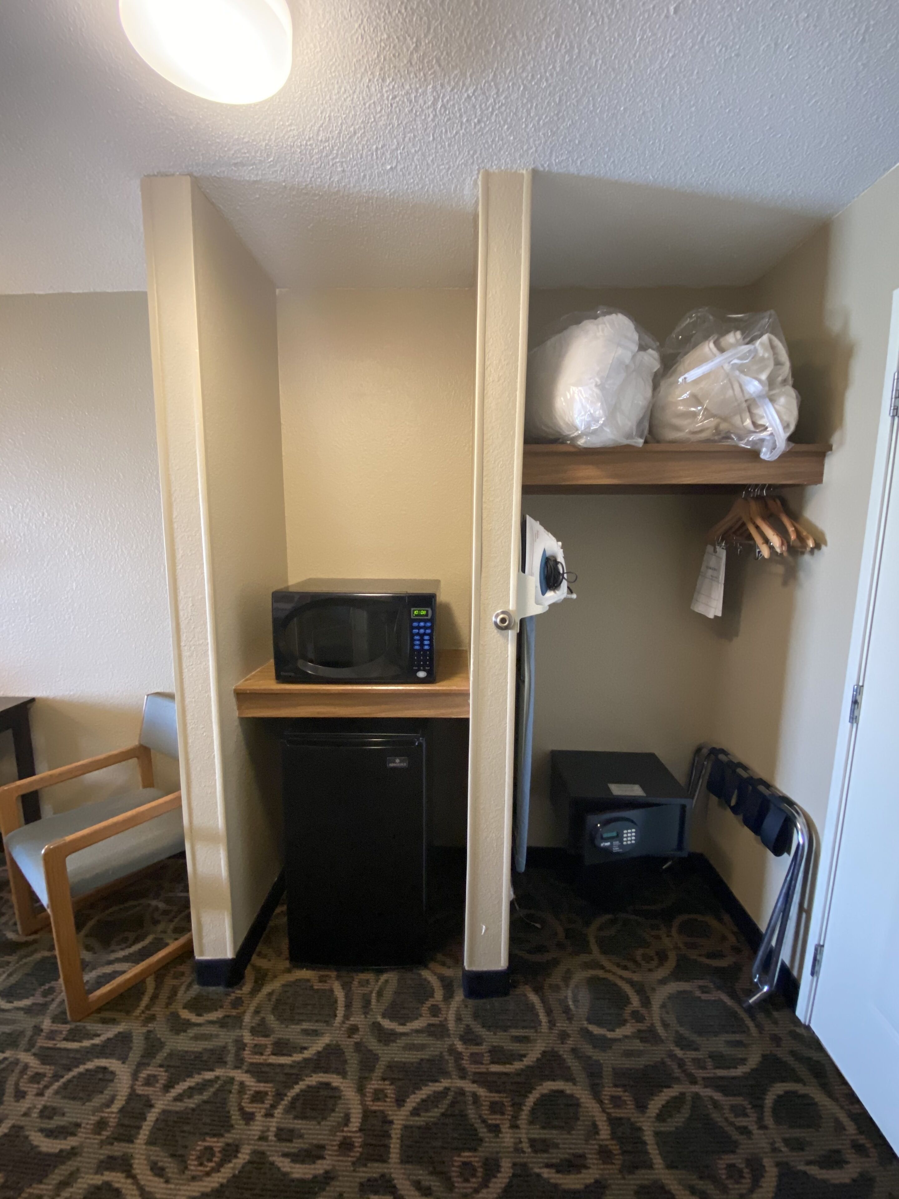 A compact kitchenette with a microwave, refrigerator, and a small shelf with bags.