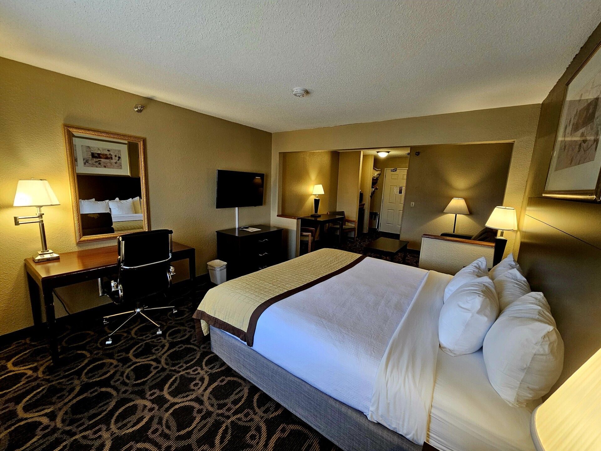 Una habitación de hotel con cama, escritorio, silla, televisor y lámparas.
