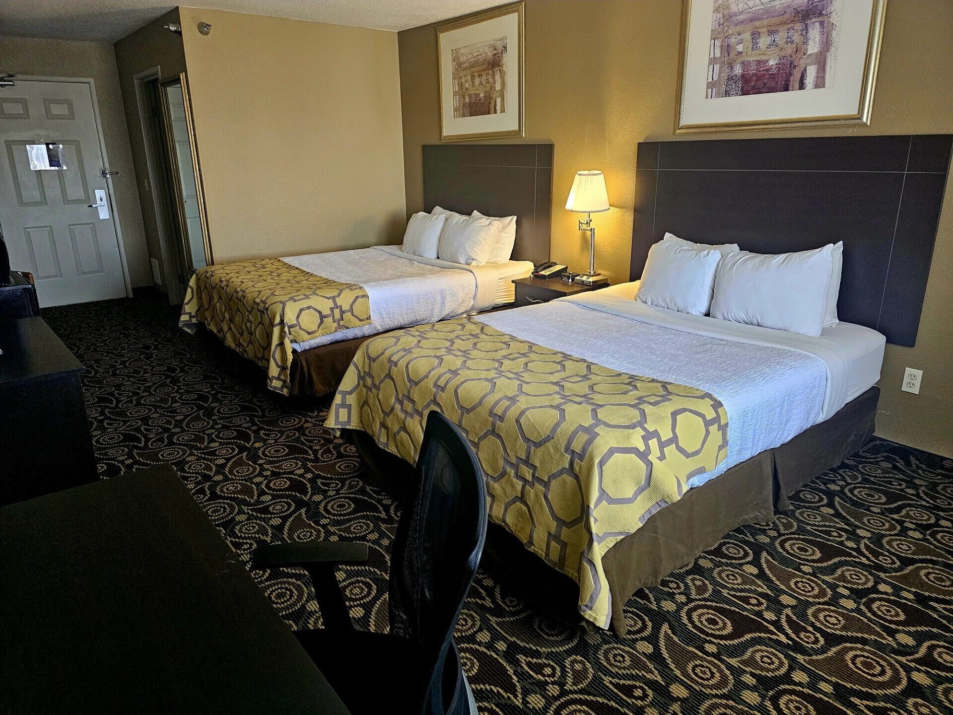 Une chambre d’hôtel avec deux lits, un bureau et une chaise. Il y a une lampe sur le bureau et un téléphone sur la table de chevet.