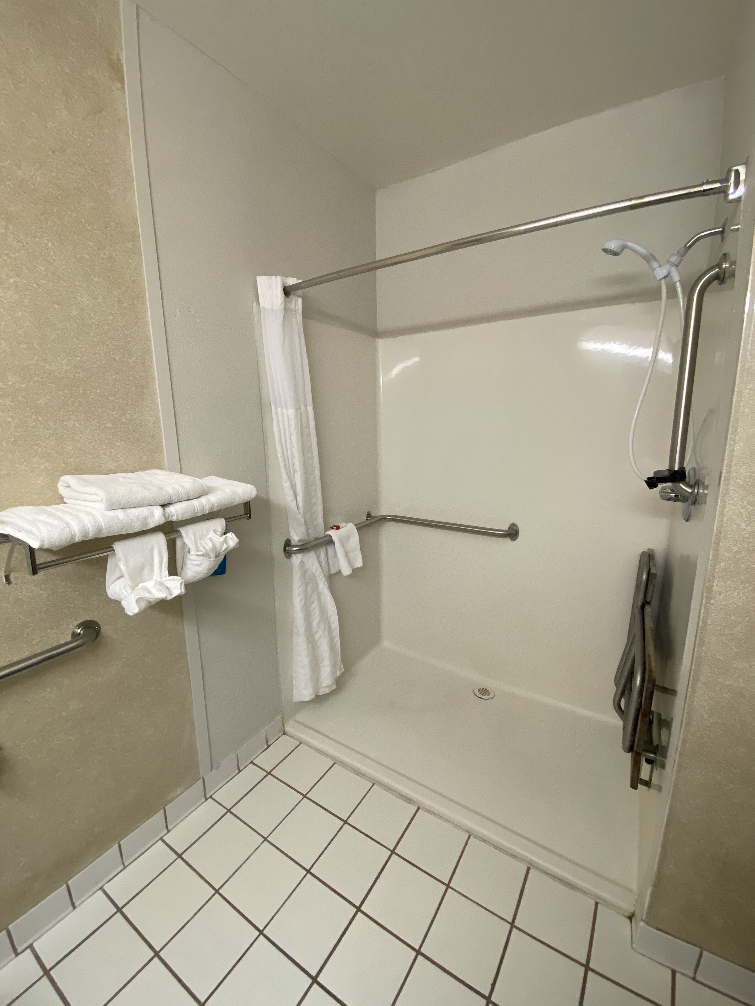 Een douche met een handgreep, een handdoekhouder met opgevouwen handdoeken, en een betegelde vloer.