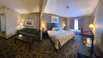 A hotel room with a bed, a sofa, a desk, and a carpeted floor.