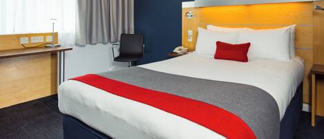 A hotel room with a bed, a desk, a chair, and a nightstand.