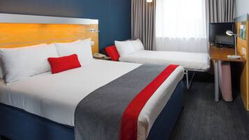 A hotel room with two beds, a desk, a TV, and a window with curtains.