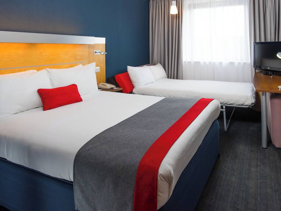 A hotel room with two beds, a desk, a TV, and a window with curtains.