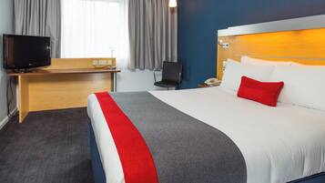 Habitación de hotel con cama, escritorio con televisor, silla y mesita de noche con teléfono.