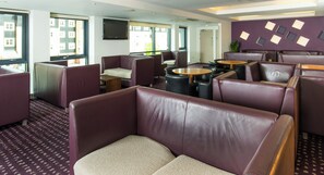 A modern hotel lobby with leather seating, a flat-screen TV, and large windows.
