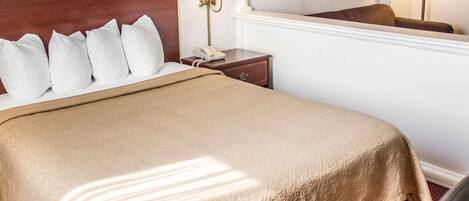 Une chambre d’hôtel avec un grand lit, une tête de lit en bois, une table de chevet avec une lampe et un téléphone.