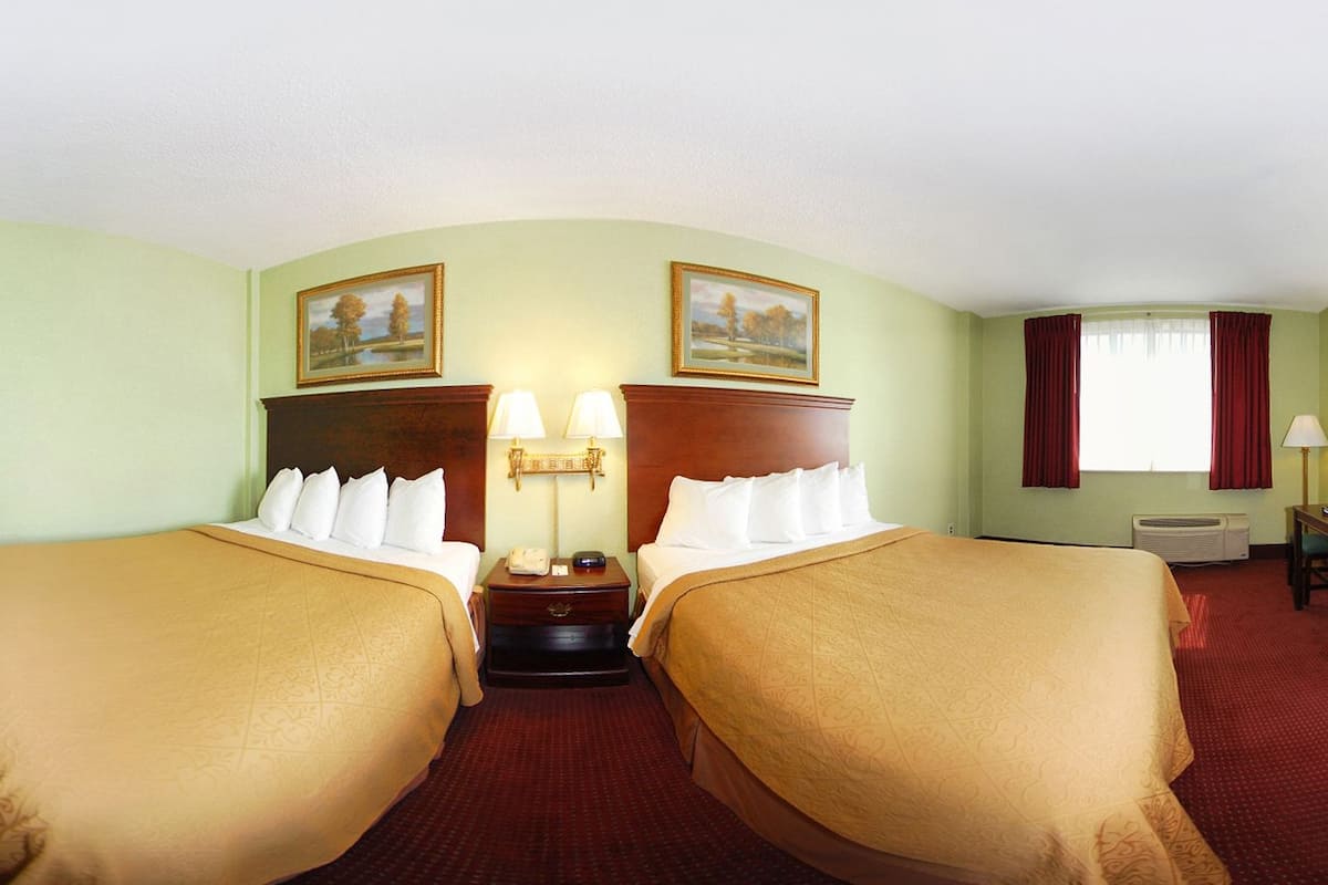 A hotel room with two beds, a nightstand, a lamp, and a painting on the wall.