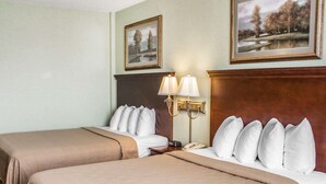 A hotel room with two beds, a nightstand with a lamp, and two framed pictures on the wall.