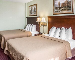 A hotel room with two beds, a nightstand with a lamp, and two framed pictures on the wall.
