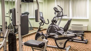 A gym with various exercise machines, a mirrored wall, and a window with blinds.