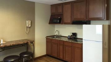 A compact kitchen with wooden cabinets, a microwave, a sink, and a refrigerator. There are two stools at a small table.