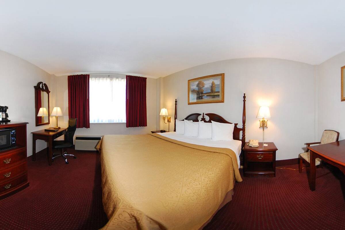 A hotel room with a large bed, a desk, a chair, a dresser, and a television.