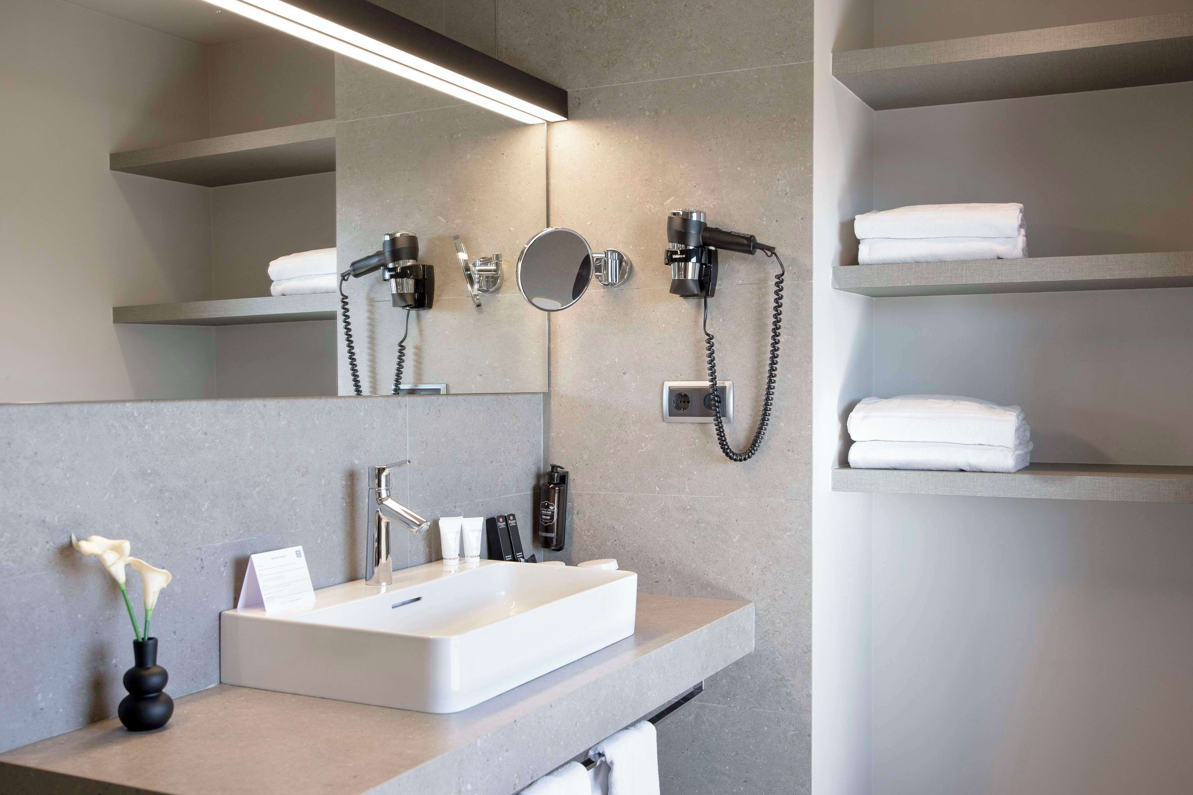 A modern bathroom with a large mirror, a white sink, and built-in towel racks.