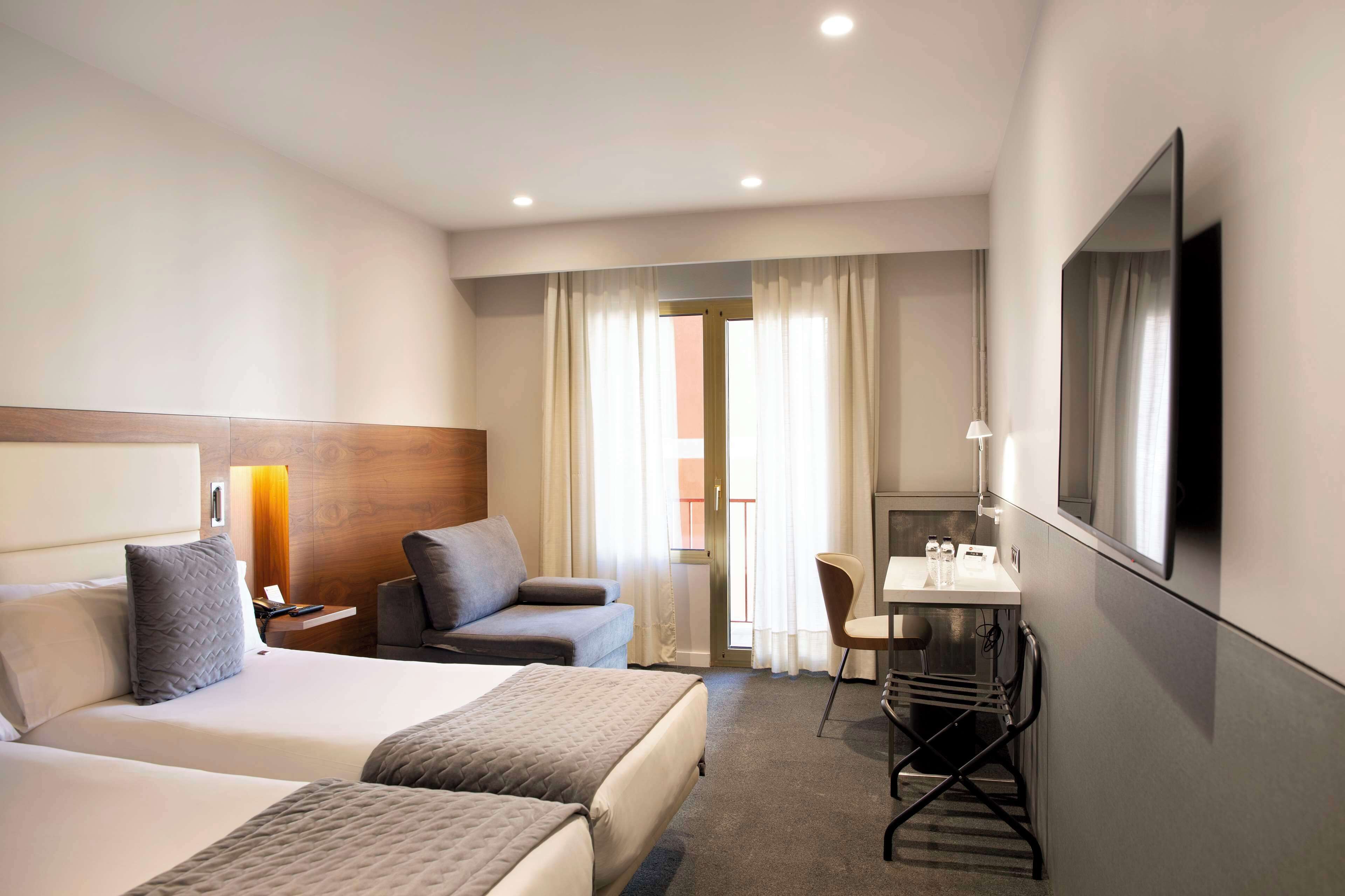 Habitación de hotel con dos camas, un escritorio, una silla, un televisor y una ventana con cortinas.