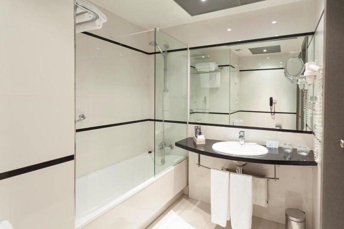 A modern bathroom with a glass-enclosed shower, a white sink with a black countertop, and a large mirror.